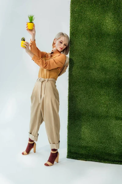 Красива стильна блондинка тримає квіткові горщики на сірій траві — стокове фото