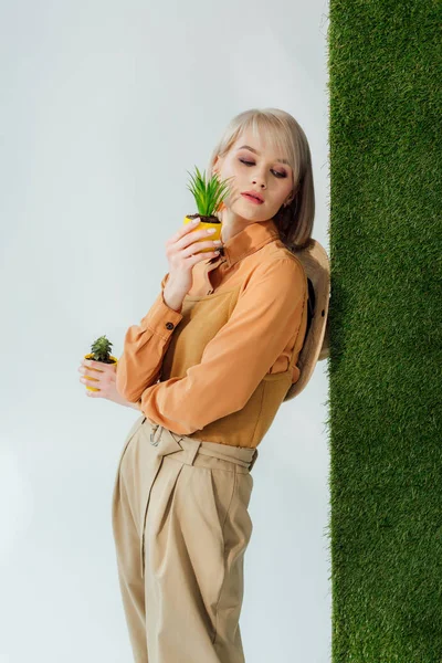 Belle fille à la mode tenant des pots de fleurs sur gris avec herbe verte — Stock Photo