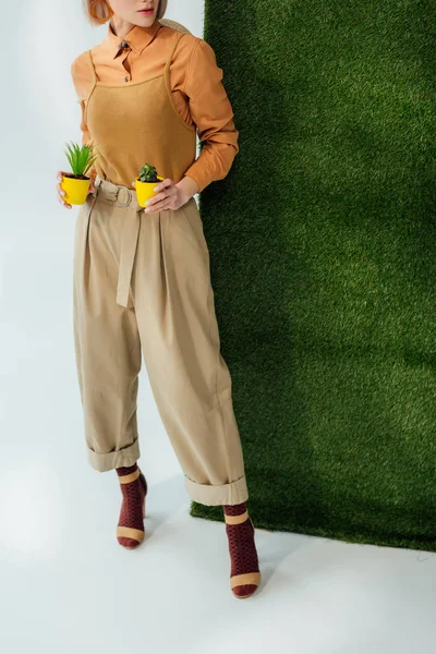 Vista recortada de chica elegante sosteniendo macetas en gris con hierba verde - foto de stock