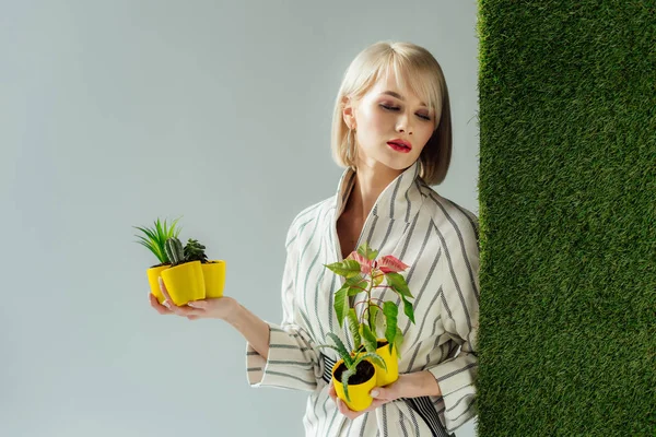 Bella elegante giovane donna che tiene vasi di fiori sul grigio con erba verde — Foto stock