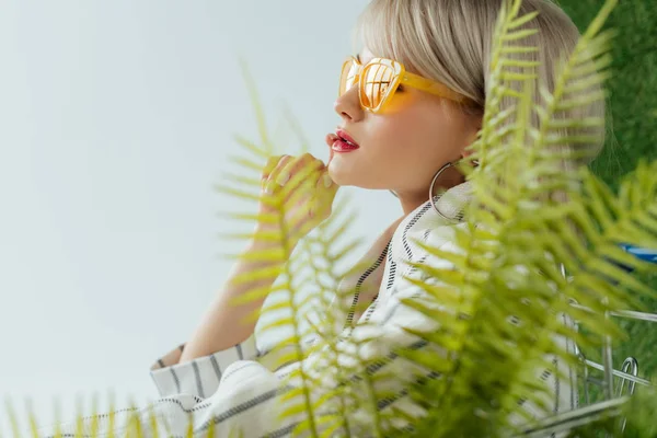 Hermosa chica con estilo en gafas de sol posando cerca de hojas de helecho con espacio de copia - foto de stock
