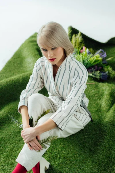 Красива стильна блондинка позує на штучній траві з листям папороті — стокове фото