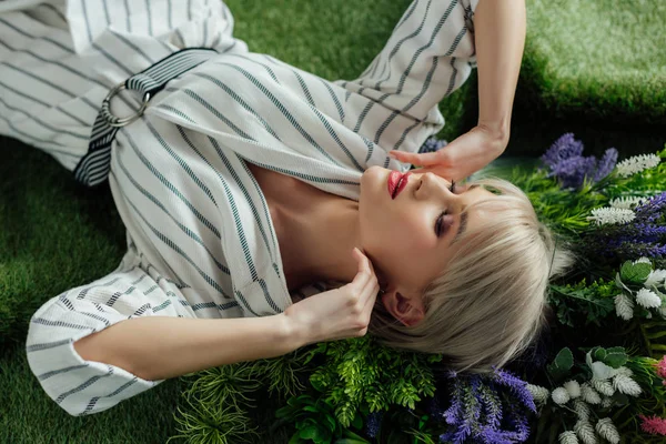 Красивая стильная девушка с закрытыми глазами позирует на искусственной траве с папоротником и цветами — стоковое фото