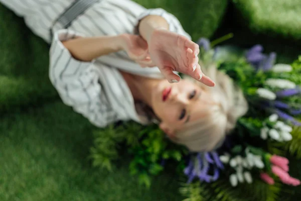 Stylish girl with outstretched hands lying on artificial grass with plants — Stock Photo