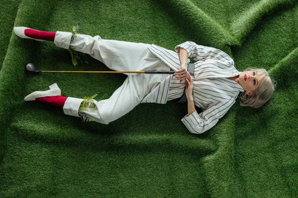 Visão de alto ângulo de bela menina elegante deitado com clube de golfe na grama artificial — Fotografia de Stock