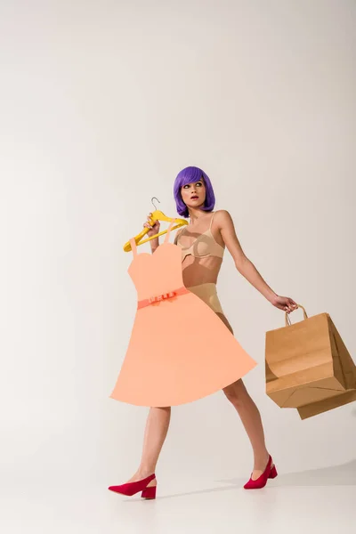 Schönes Mädchen mit lila Haaren mit Papierkleid und Einkaufstaschen auf weißem Grund — Stockfoto