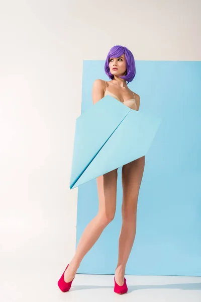 Hermosa joven con el pelo morado posando con avión de papel en azul y blanco — Stock Photo