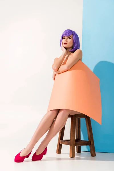 Menina bonita com cabelo roxo coberto de folha de papel de coral sentado na cadeira enquanto posando em azul e branco — Fotografia de Stock