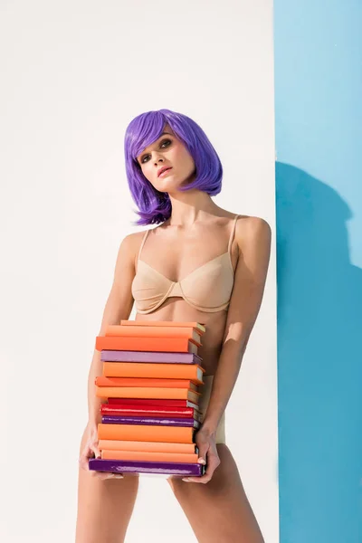 Красива дівчина з фіолетовим волоссям дивиться на камеру і тримає барвисті книги на синьому і білому — стокове фото