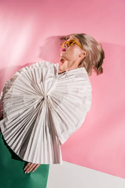 Hermosa chica con estilo en gafas de sol y ropa de papel en rosa y blanco - foto de stock