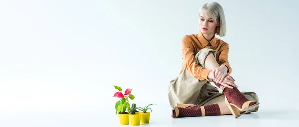 Panoramic shot of beautiful stylish girl sitting with flower pots on white with copy space — Stock Photo