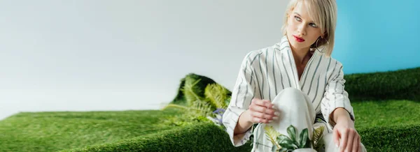 Panoramic shot of beautiful stylish blonde girl sitting on artificial grass — Stock Photo
