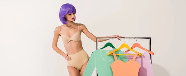 Plan panoramique de belle fille aux cheveux violets posant près de rack avec des vêtements en papier sur blanc — Photo de stock