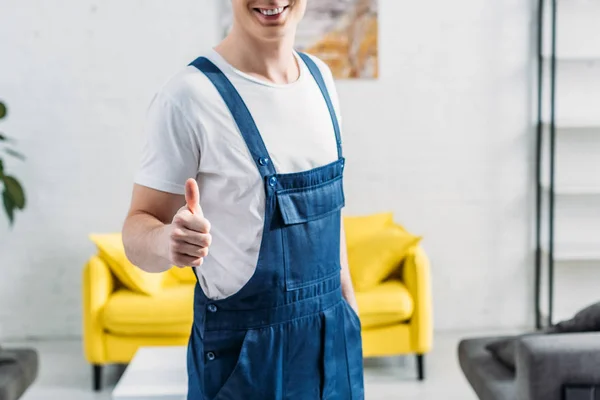 Vue recadrée du déménageur en uniforme montrant le pouce vers le haut signe dans l'appartement — Photo de stock