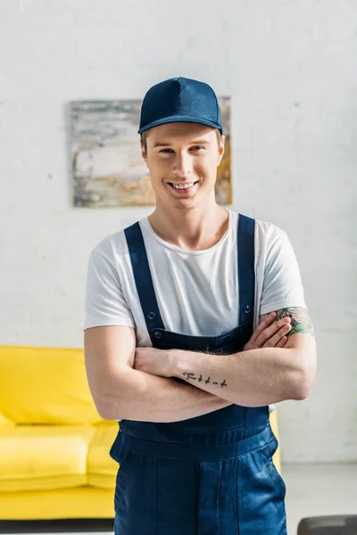 Beau déménageur avec les bras croisés regardant la caméra et souriant dans l'appartement — Photo de stock