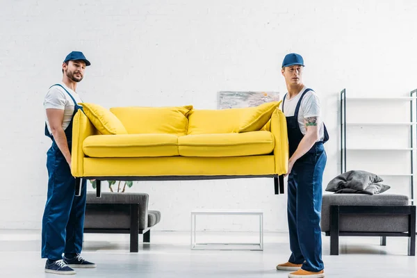 Two movers in uniform transporting couch in apartment — Stock Photo