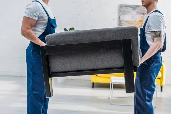 Vista recortada de dos mudanzas en uniforme transportando muebles en apartamento - foto de stock