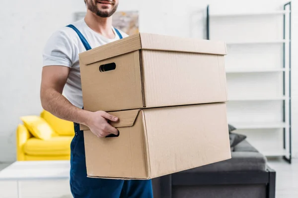 Cropped view of mover in uniform carrying cardboard boxes in apartment — Stock Photo