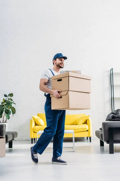 Déménageur en uniforme portant des boîtes en carton dans un appartement moderne — Photo de stock