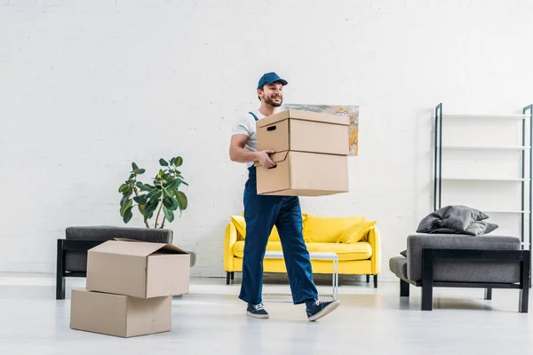 Déménageur en uniforme portant des boîtes en carton dans un appartement moderne — Photo de stock