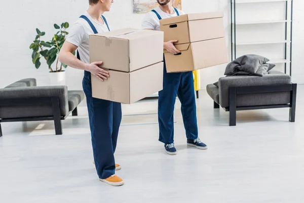 Cropped view of two movers in uniform carrying cardboard boxes in apartment — Stock Photo