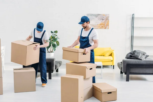 Dos mudanzas en uniforme llevando cajas de cartón en apartamento moderno - foto de stock