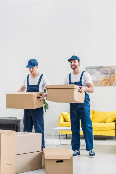 Two movers in uniform transporting cardboard boxes in apartment — Stock Photo