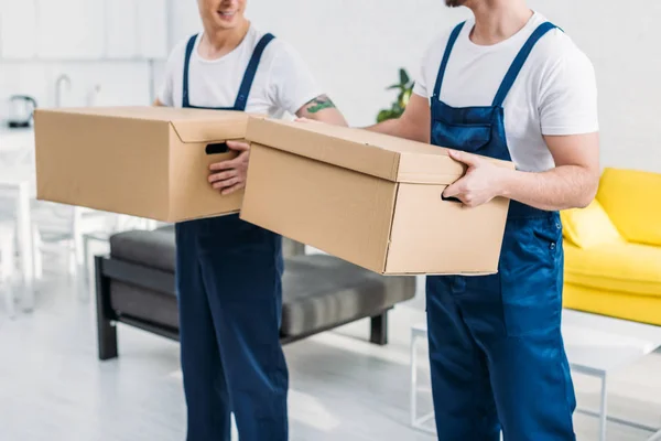 Cropped view of two movers transporting cardboard boxes in apartment — Stock Photo