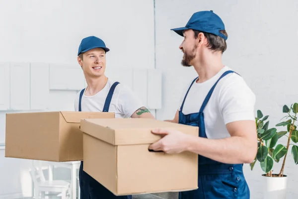 Due traslocatori sorridenti che trasportano scatole di cartone in appartamento — Foto stock