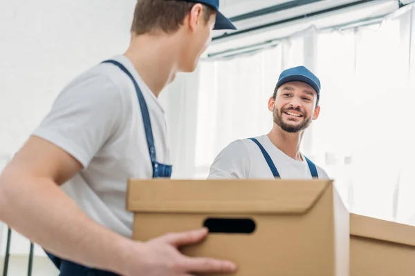 Selective focus of two movers transporting cardboard boxes in apartment — Stock Photo