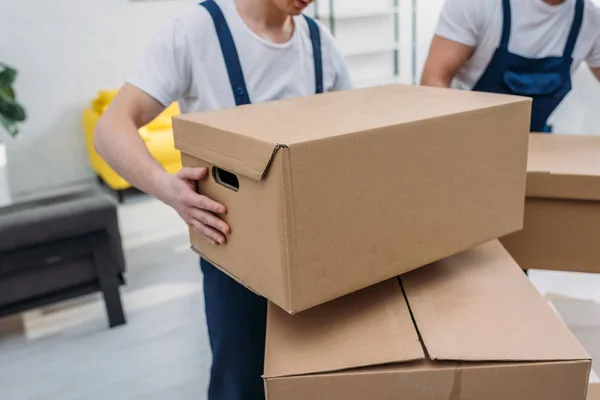 Cropped view of two movers transporting cardboard boxes in apartment — Stock Photo