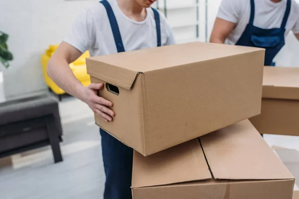 Vista recortada de dos mudanzas que transportan cajas de cartón en el apartamento - foto de stock