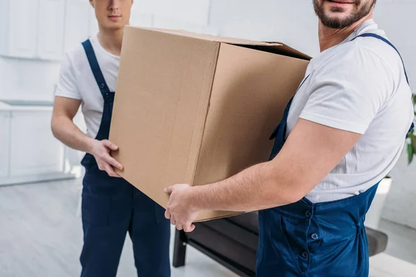 Partial view of two movers transporting cardboard box in apartment — Stock Photo