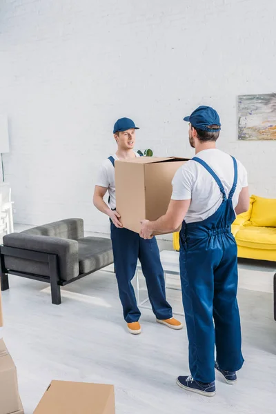 Two movers in uniform transporting cardboard box in living room — Stock Photo