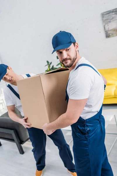 Zwei Umzugshelfer in Uniform transportieren Karton in Wohnung — Stockfoto