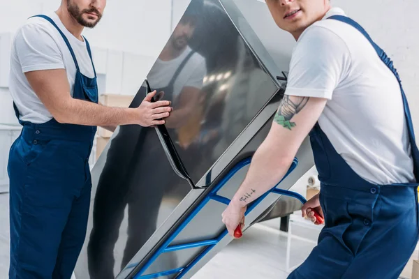 Cropped view of two movers using hand truck while transporting refrigerator in apartment — Stock Photo