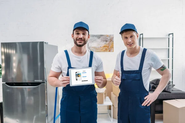 Two movers presenting digital tablet with instagram app on screen and showing thumb up sign in apartment — Stock Photo