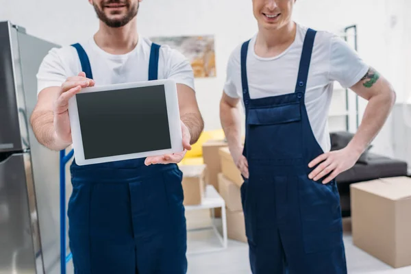 Vista ritagliata di due traslocatori che presentano tablet digitale con schermo bianco in appartamento — Foto stock