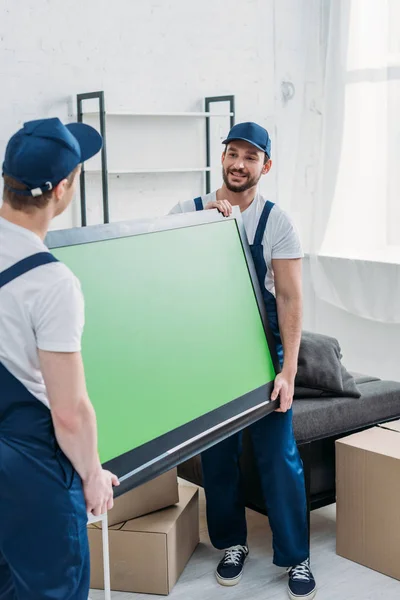 Dois movers transportando tv com tela verde no apartamento — Fotografia de Stock