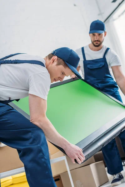 Due traslocatori in uniforme che trasportano tv con schermo verde in appartamento — Foto stock