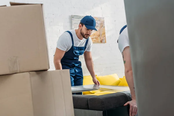 Selektiver Fokus der Mover, die Möbel mit einer Rolle Stretchfolie in der Wohnung umwickeln — Stockfoto