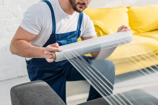 Vista recortada de mover muebles de envoltura con rollo de película estirable en el apartamento - foto de stock