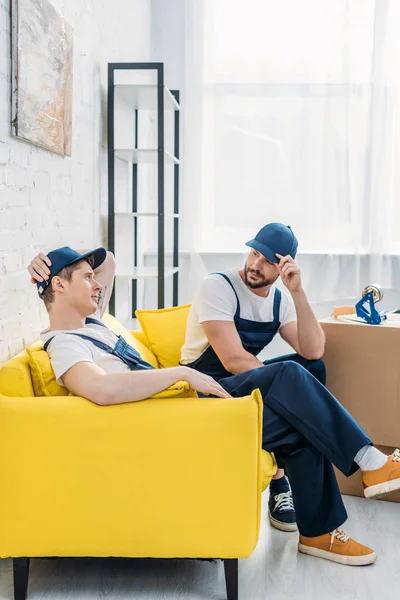 Deux déménageurs en uniforme assis sur le canapé dans l'appartement — Photo de stock