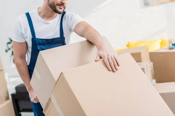 Cropped view of mover in uniform transporting cardboard boxes in apartment — Stock Photo