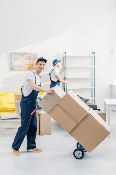 Deux déménageurs en uniforme transportant des boîtes en carton et des meubles dans l'appartement — Photo de stock