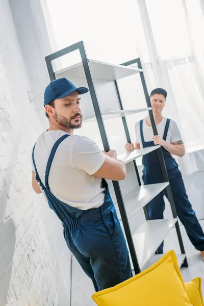 Two handsome movers in uniform transporting rack in apartment — Stock Photo