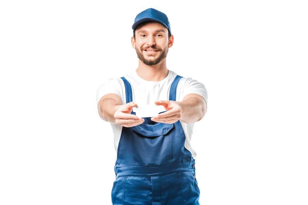 Smiling handsome mover in uniform looking at camera and holding blank business card isolated on white — Stock Photo