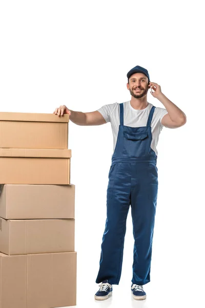 Beau déménageur souriant avec des boîtes en carton parlant sur smartphone isolé sur blanc — Photo de stock