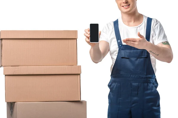 Vista recortada de mover sonriente con cajas de cartón presentando teléfono inteligente con pantalla en blanco aislado en blanco - foto de stock