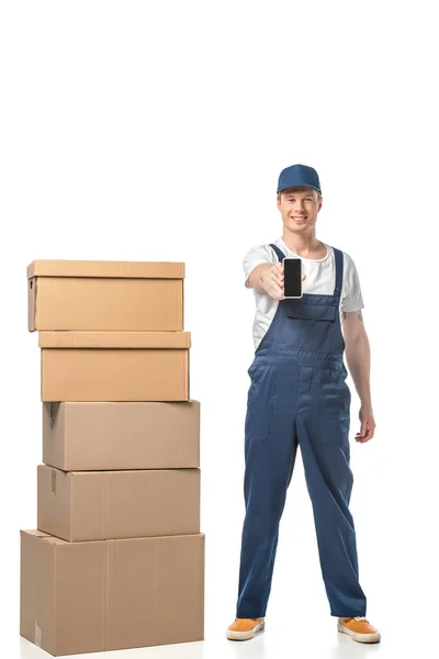 Smiling mover with cardboard boxes showing smartphone with blank screen isolated on white — Stock Photo